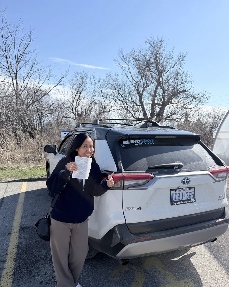 Student beside the Blindspot Driving Academy car, holding their road test result
