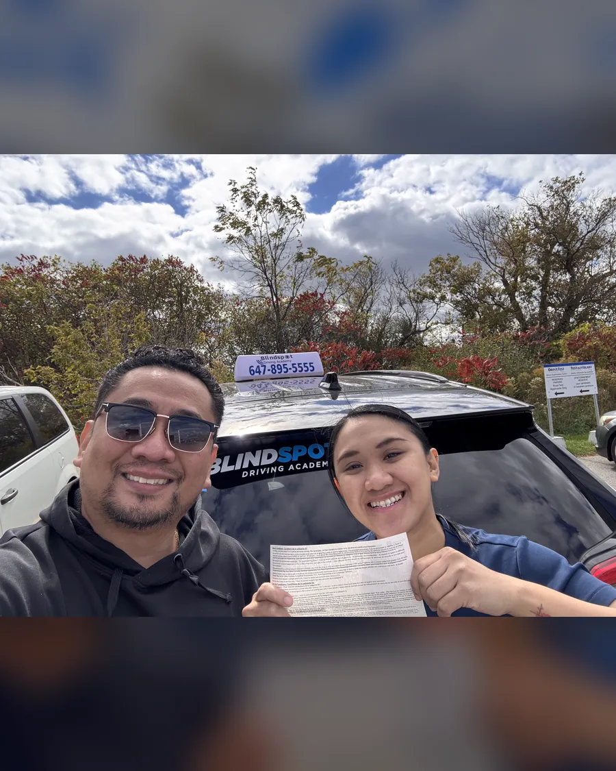 Student and instructor Allan beside the Blindspot Driving Academy car, holding a road test result