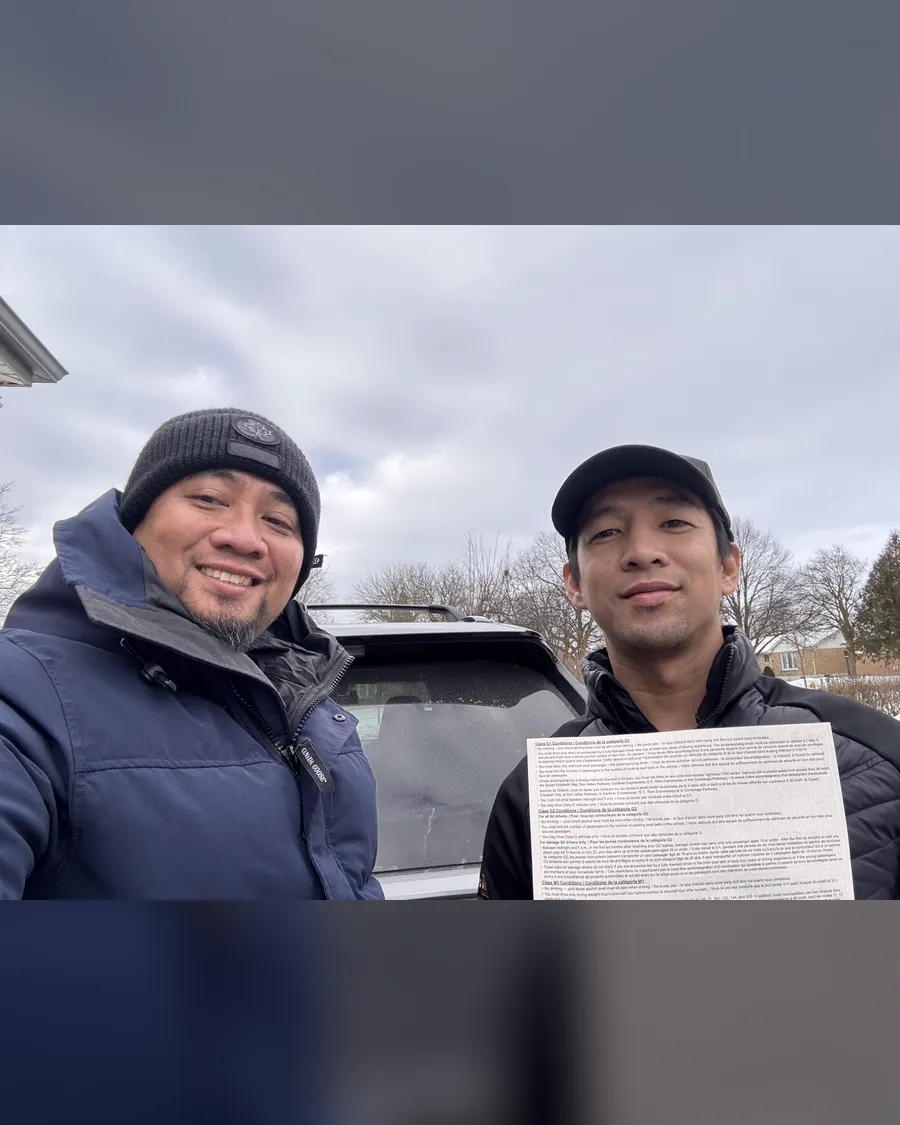 Student and instructor Allan in winter coats beside the car, holding a road test result