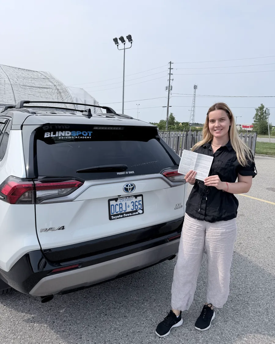 Student beside the Blindspot Driving Academy car, holding their road test result