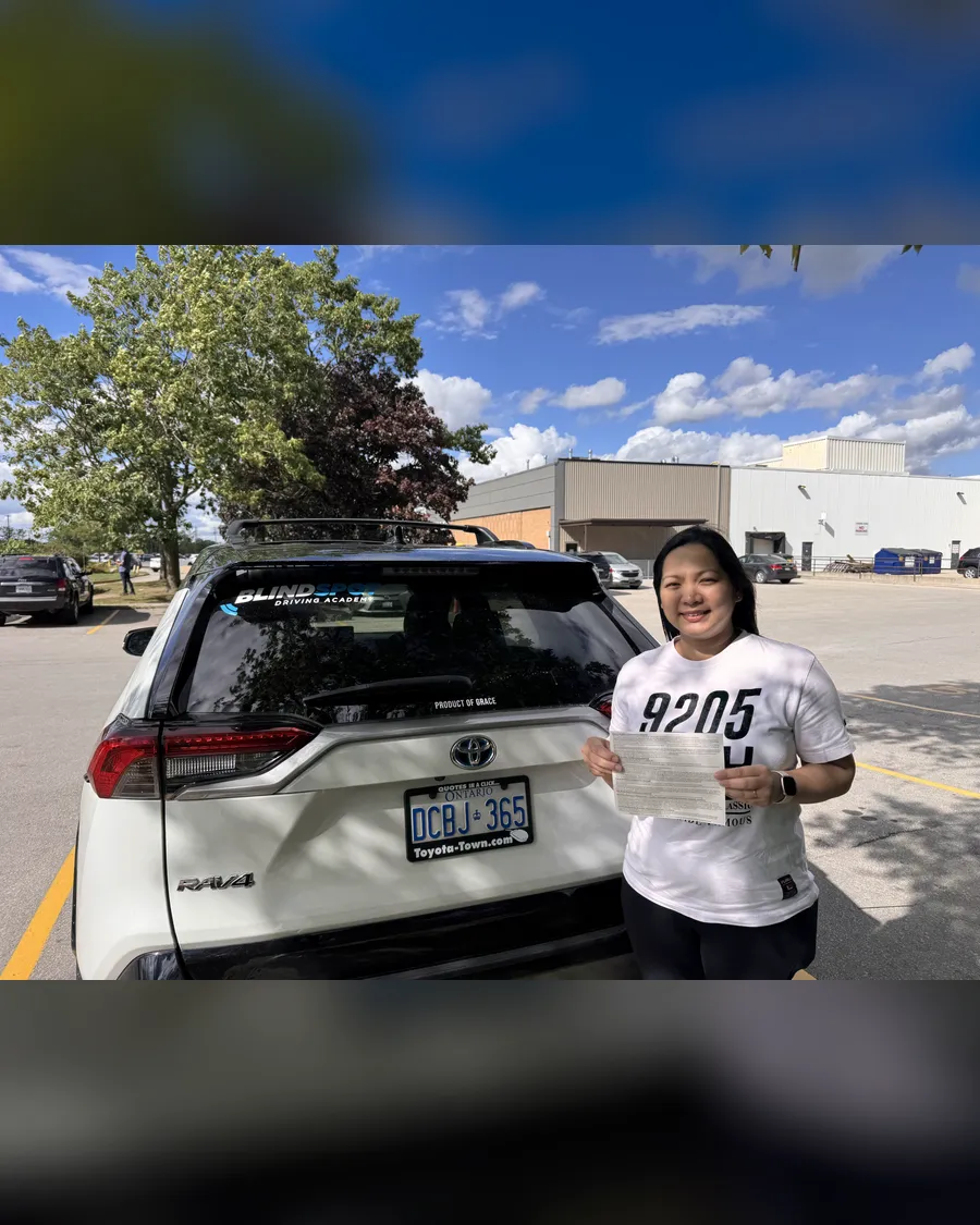Student in a white top beside the Blindspot Driving Academy car, holding their road test result