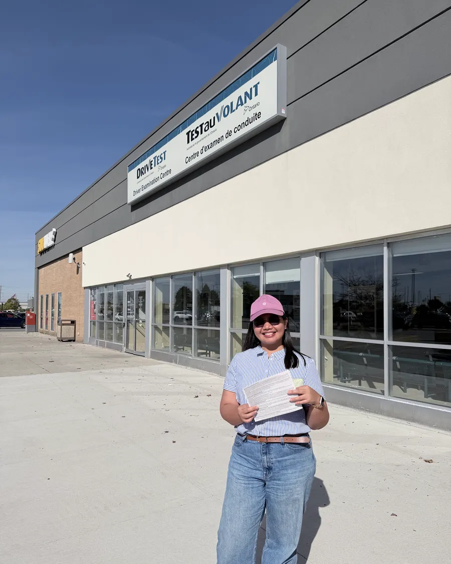 Student in a pink cap outside the DriveTest centre, holding their road test result