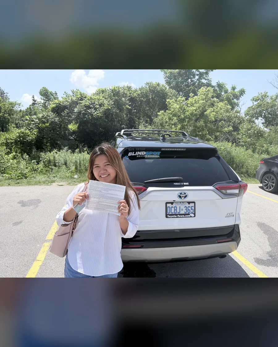 Student in a white blouse beside the Blindspot Driving Academy car, holding their road test result