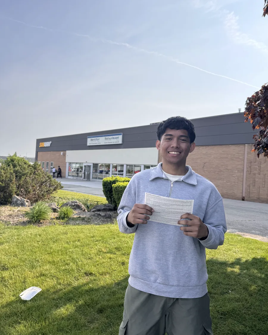 Student in a grey hoodie outside the DriveTest centre, holding their road test result