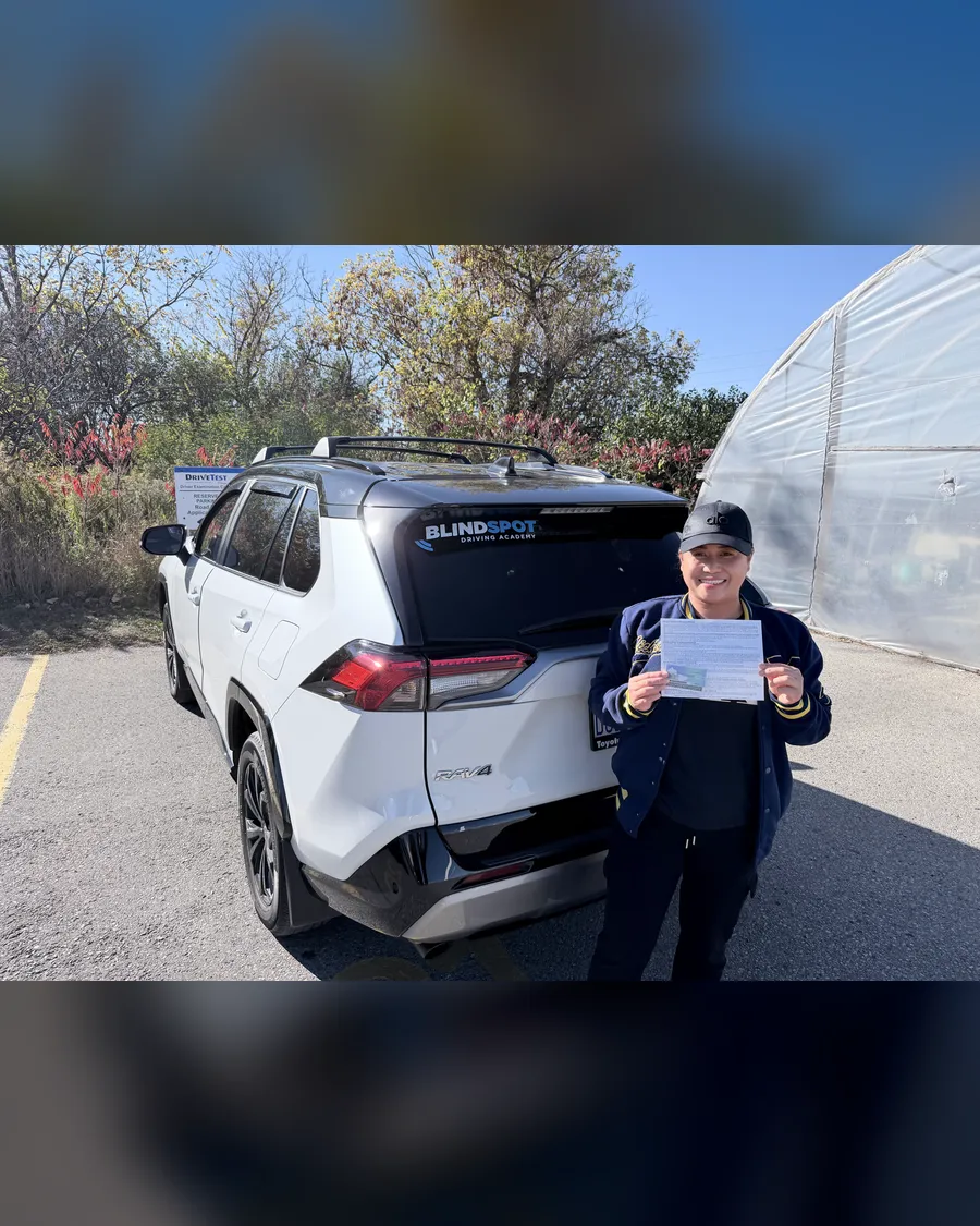 Student in a dark uniform beside the Blindspot Driving Academy car, holding their road test result