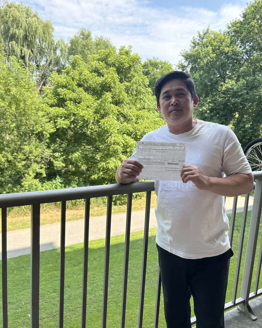 Student in a cream shirt outdoors, holding their road test result