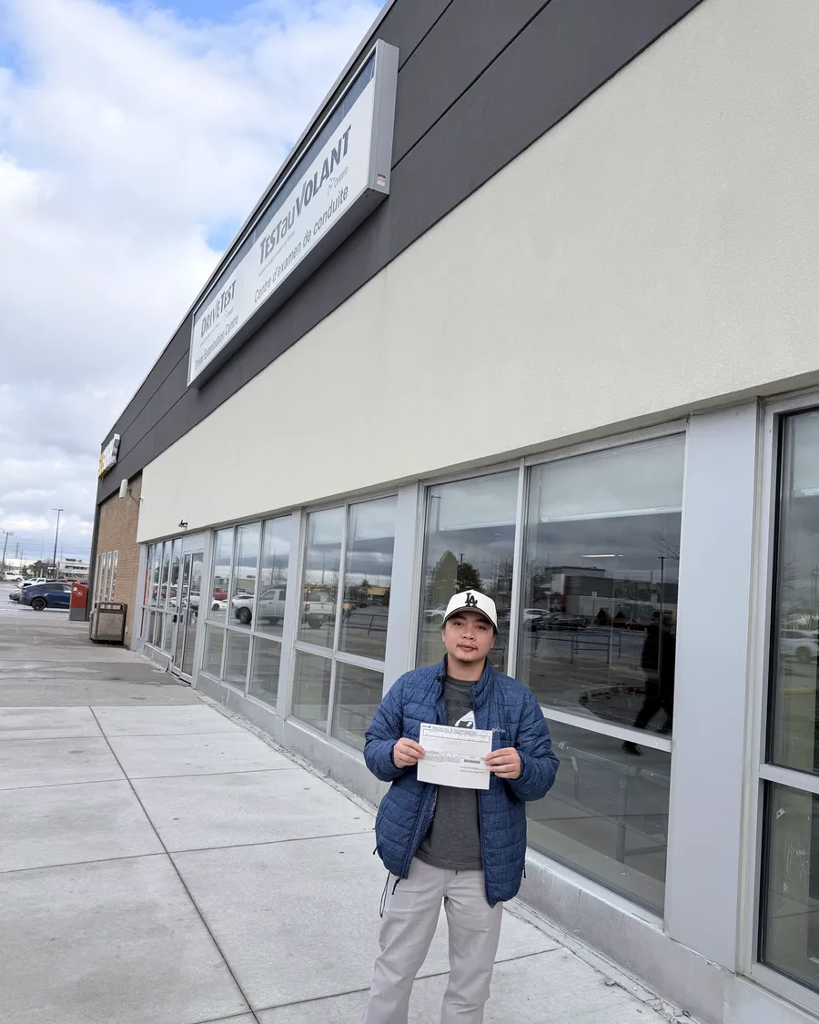 Student in a blue jacket outside the DriveTest centre, holding their road test result