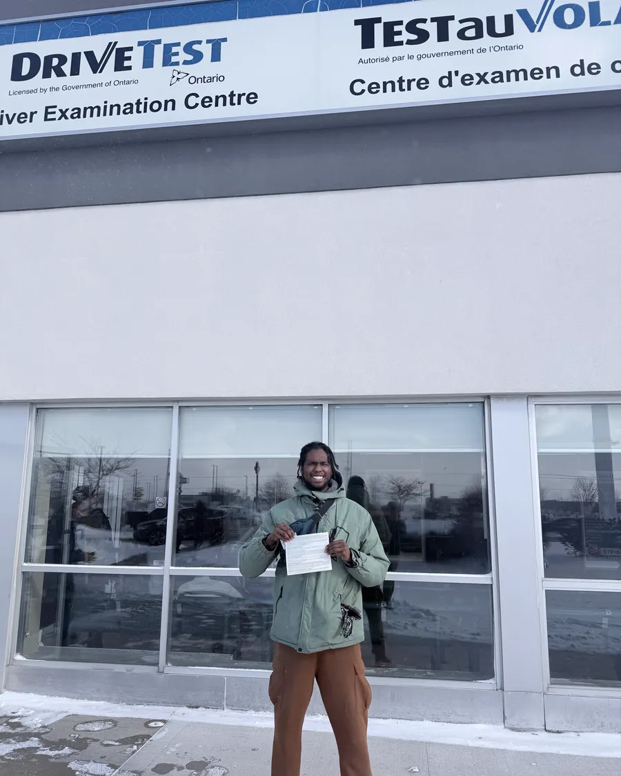 Student in a green jacket outside the DriveTest Driver Examination Centre, holding their road test result